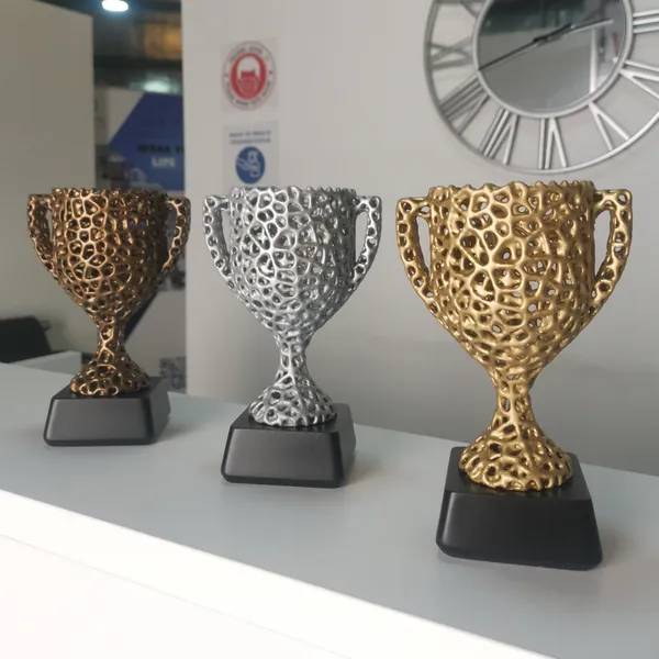 Three lattice-pattern trophy cups in bronze, silver and gold finishes on black bases