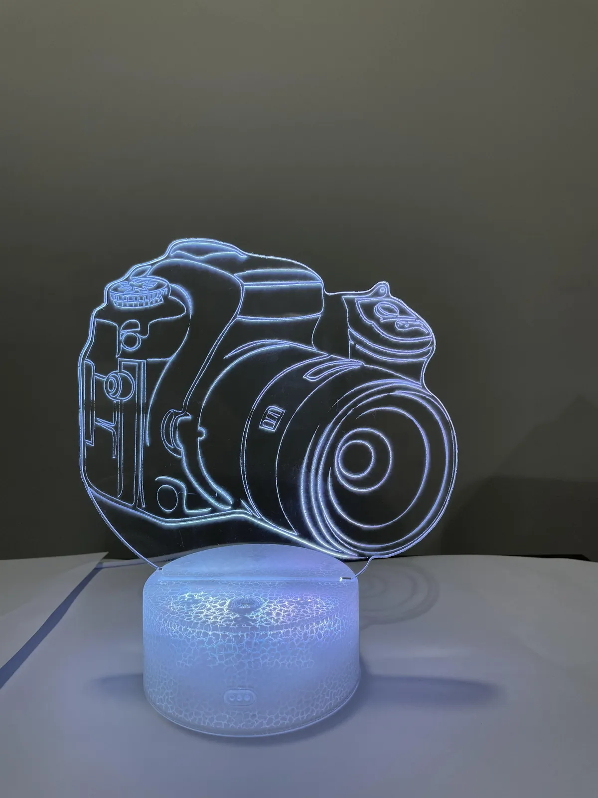 Clear acrylic panel with a line-art camera engraved into it, mounted on an illuminated base